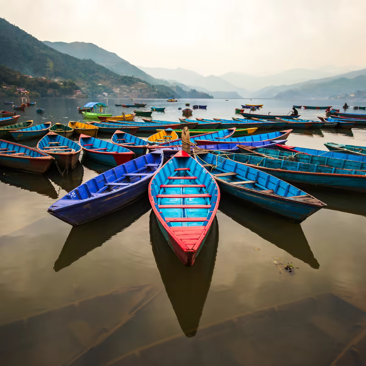 A wooden boat on Phewa Lake with Machhapuchhre reflected in the water.