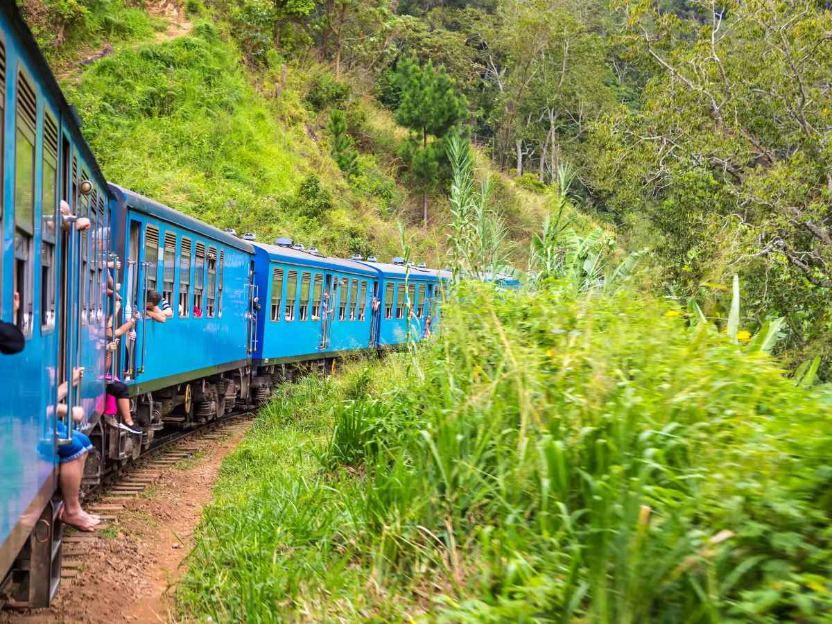 A blue train moving through Sri Lanka's green highland hills.