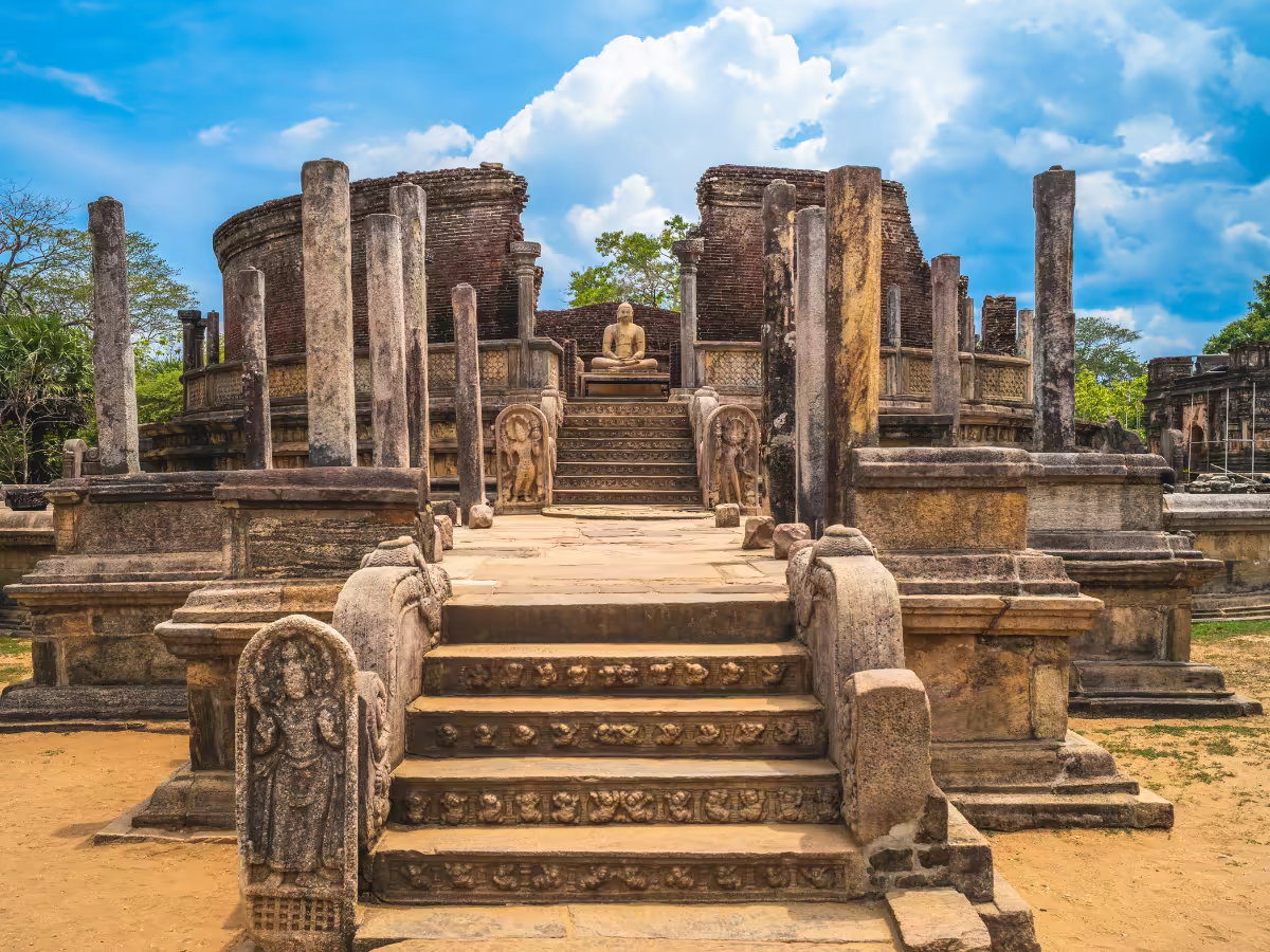 A weathered stone Buddha among palms in Polonnaruwa.